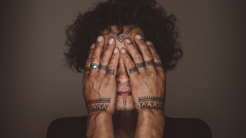 A woman covers her eyes with tattooed hands