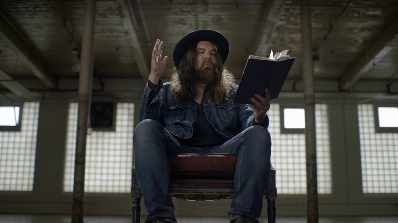 Man with a beard and hat reading a book