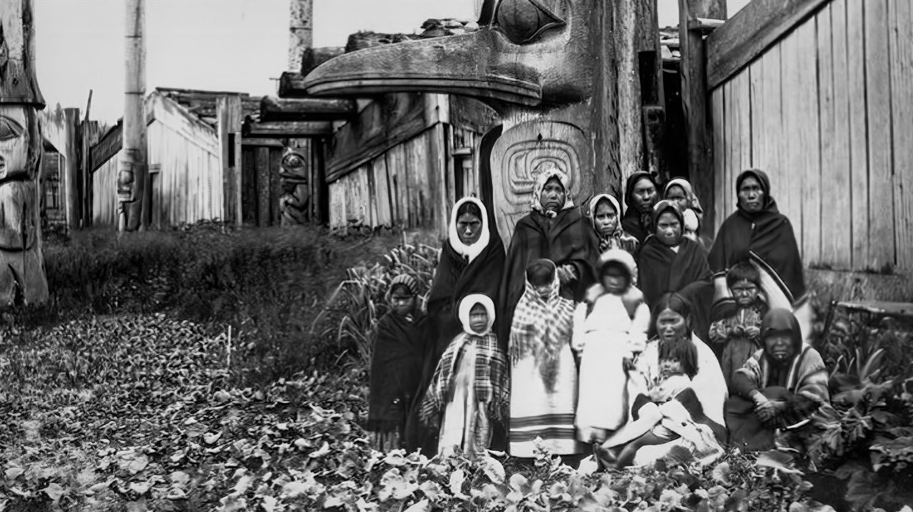 A group of Haida people in front of a totem pole