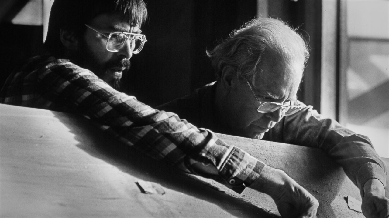 Two men with glasses leaning over a wooden plank