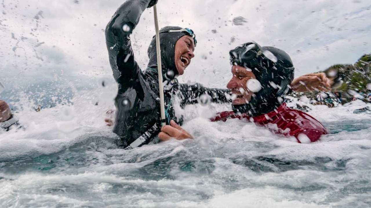 two people in wetsuits smiling in the water