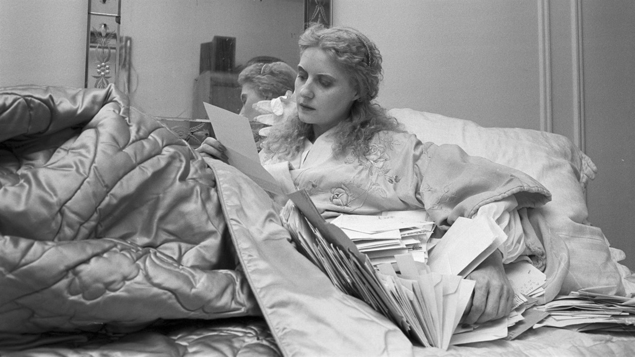 A woman sitting up in bed with many letters beside