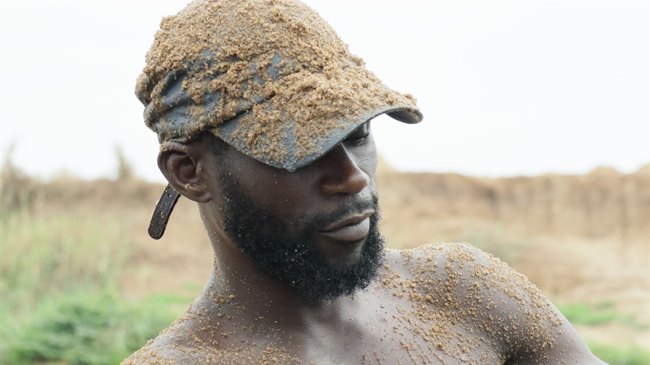Closeup of a man in a baseball cap covered in sand