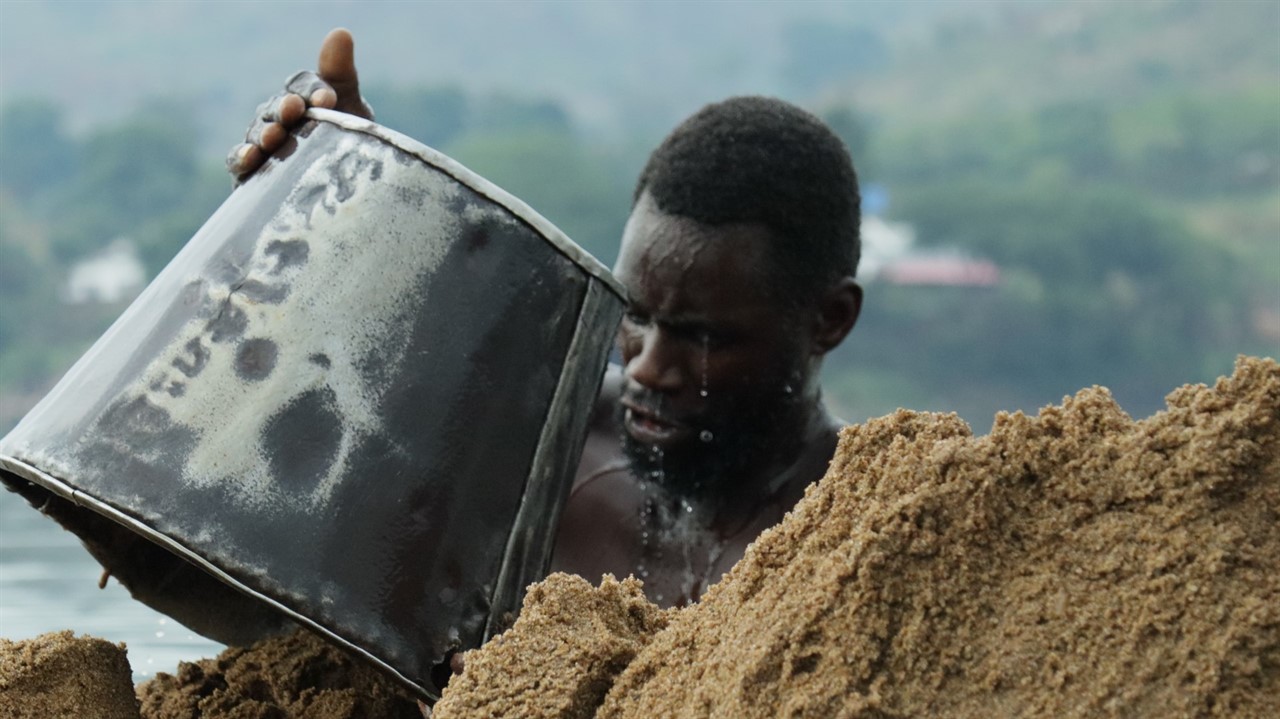 A man dumps a bucket of sand on a giant sand pile