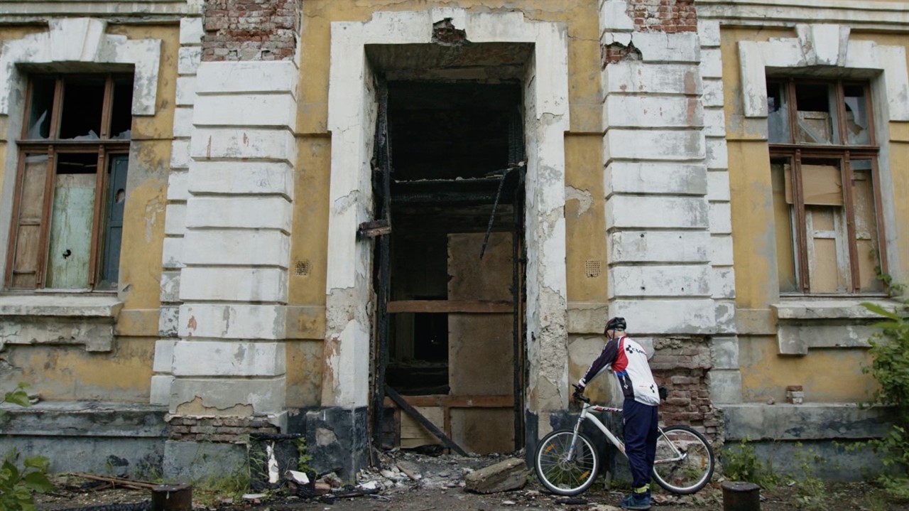 Man with bike stands outside a derelict building
