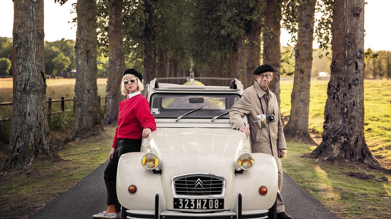 Woman and man in berets posing by a car