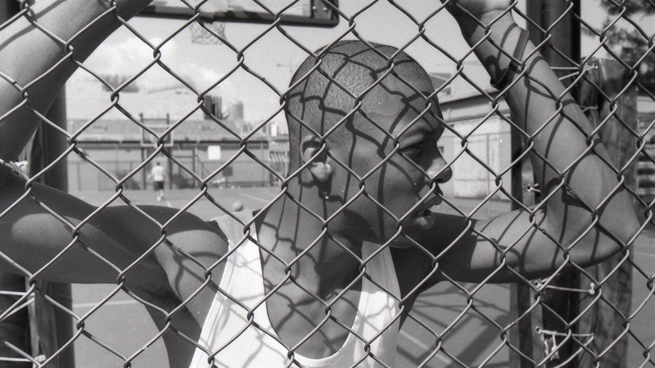 Teenage boy looking through a chain link fence