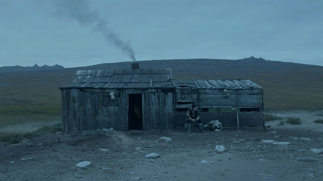 Man sitting in front of hut in barren landscape