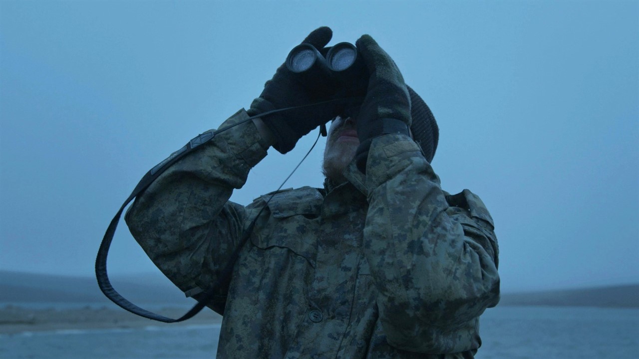 Man in camo looking up through binoculars