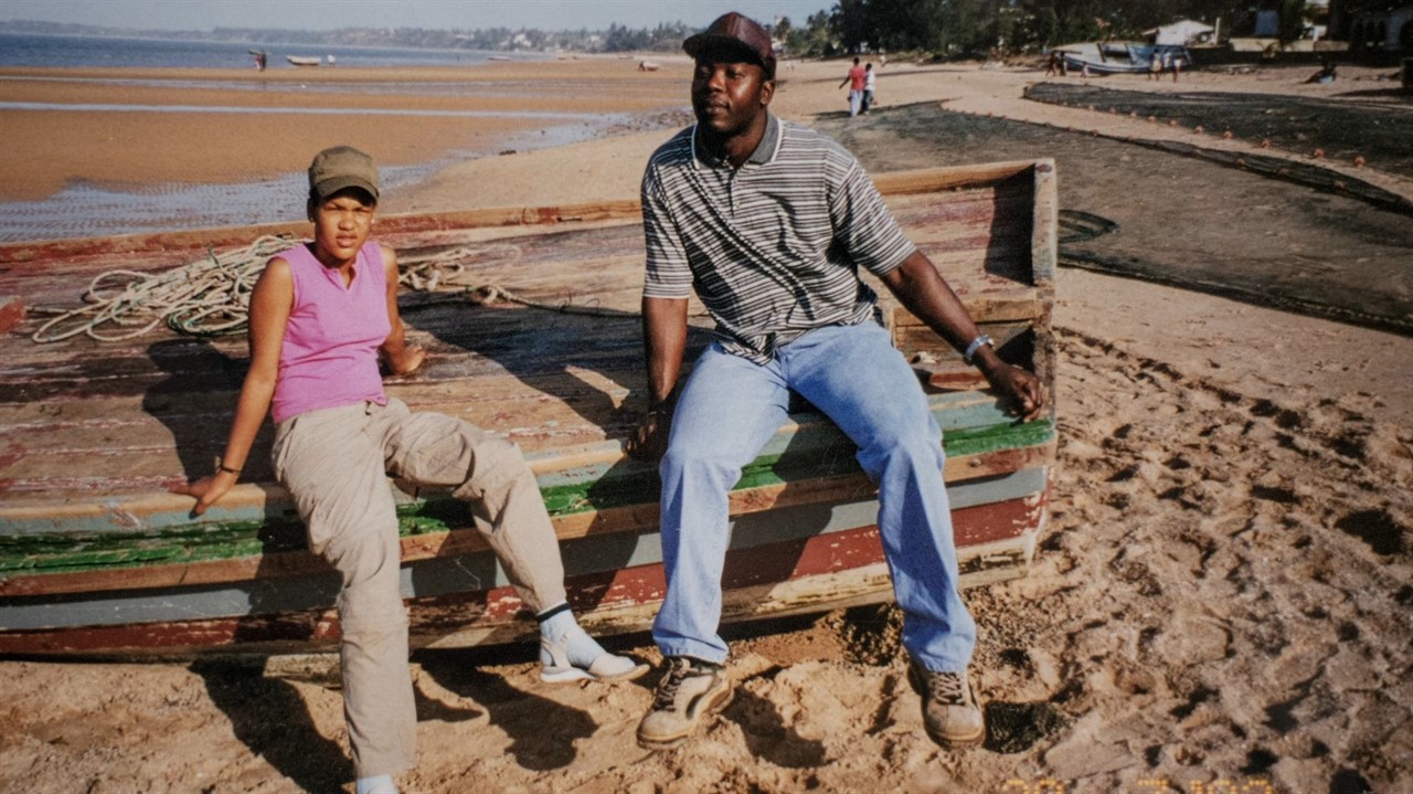 A man and teenager sit on a wooden boat on a beach