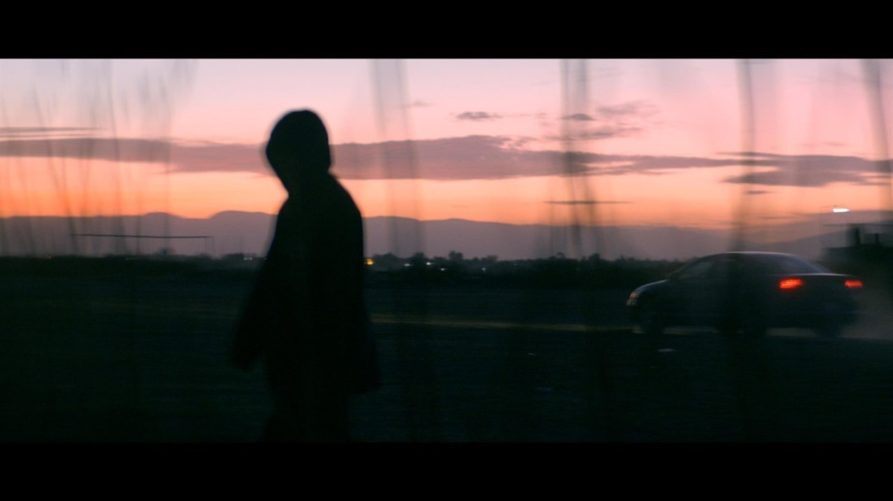 Silhouette at dusk of hooded person, car driving b