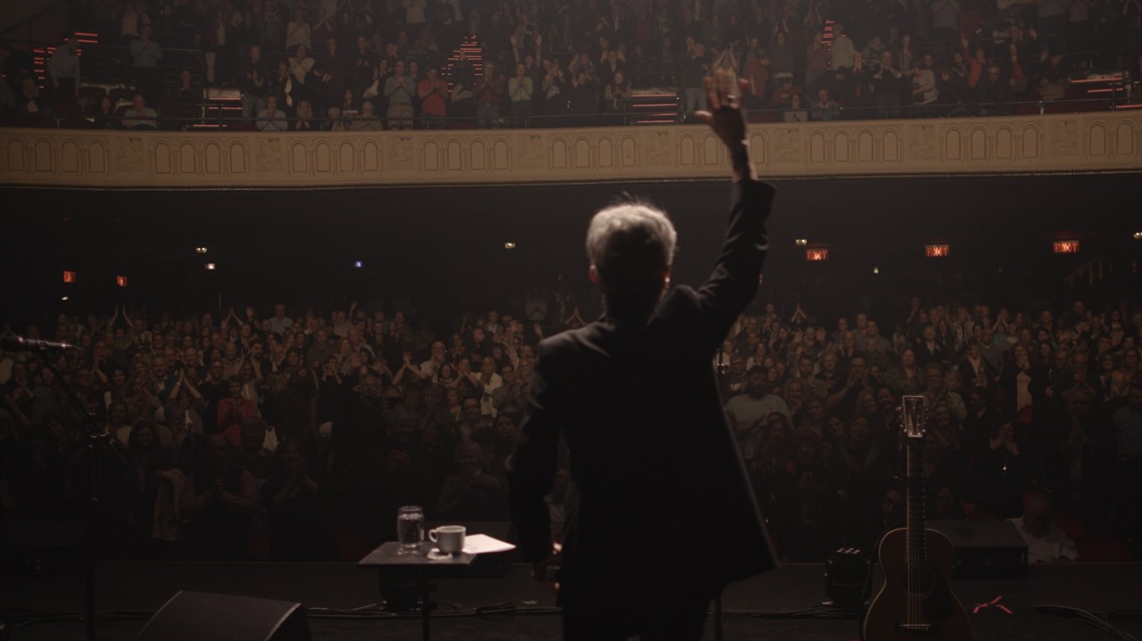 Joan Baez seen from behind waving from stage to a 