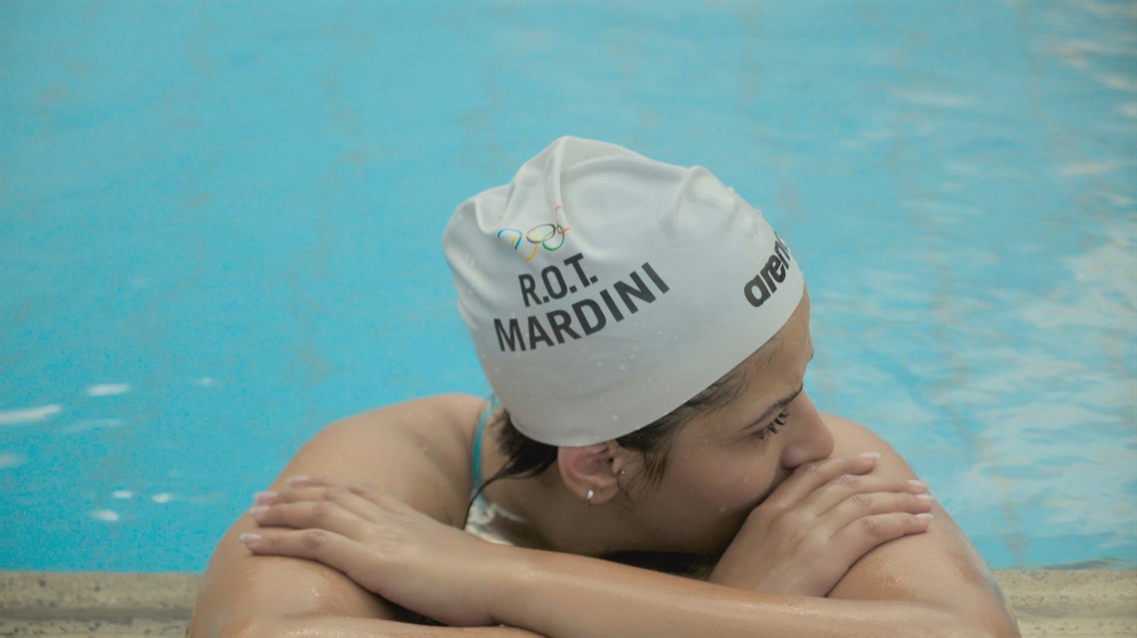 A woman in a swim cap (says R.O.T. Mardini) hang o
