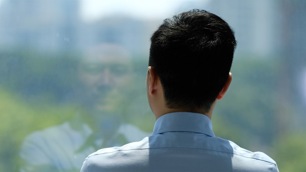 Asian man staring out window with reflection