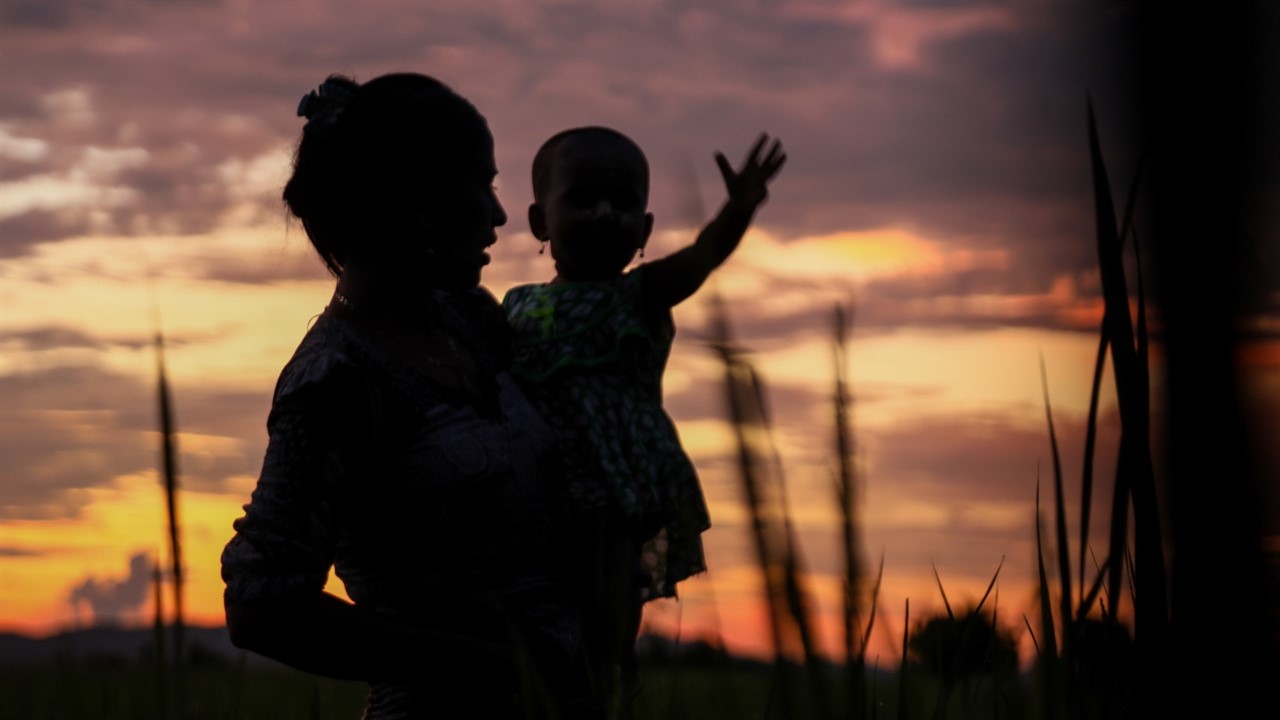 Woman holding small child in sunset