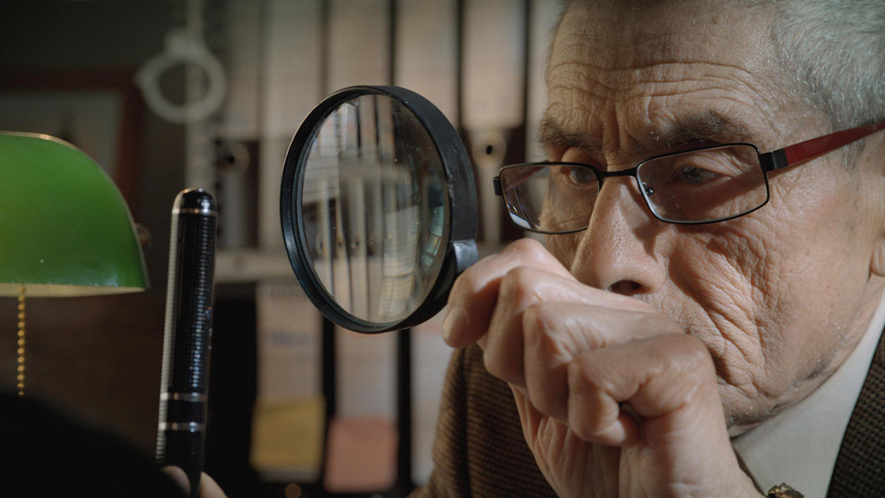 Old man in glass peering through magnifying glass