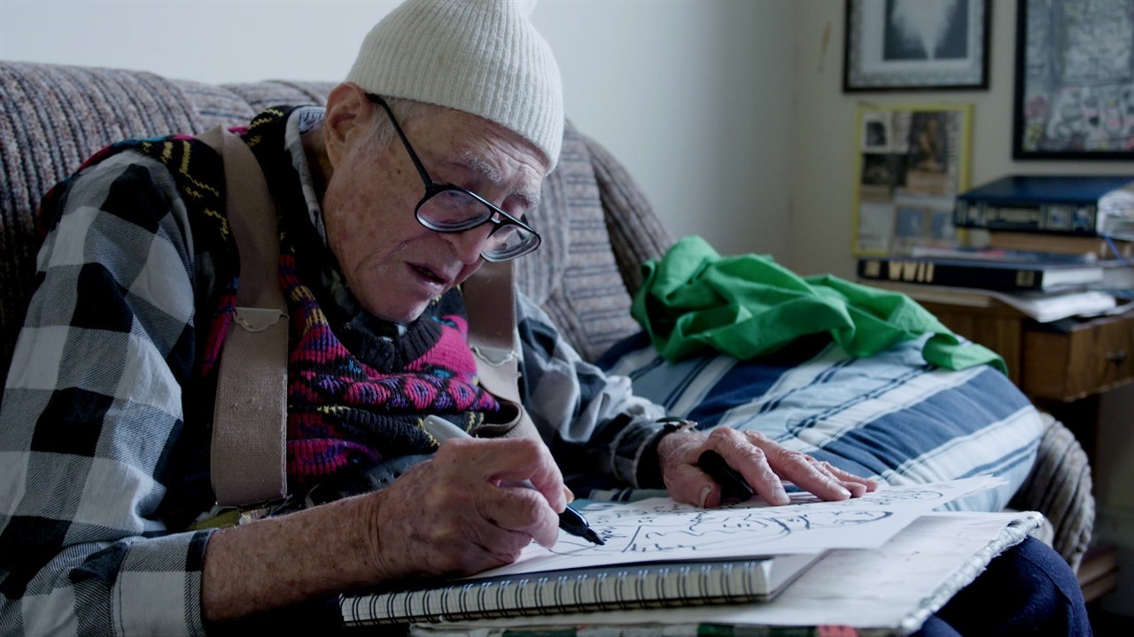 Elderly man in toque draws with Sharpie marker