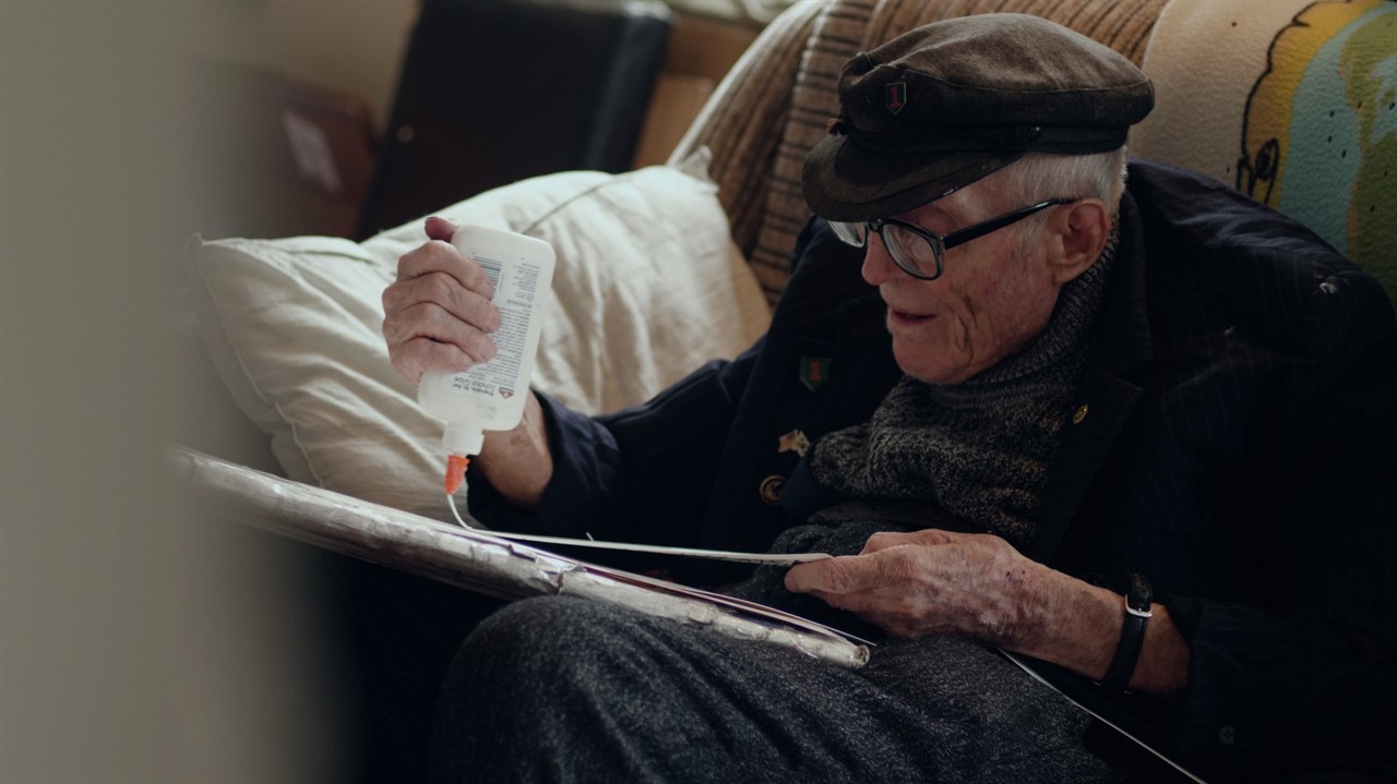 An elderly man sitting on a couch gluing something