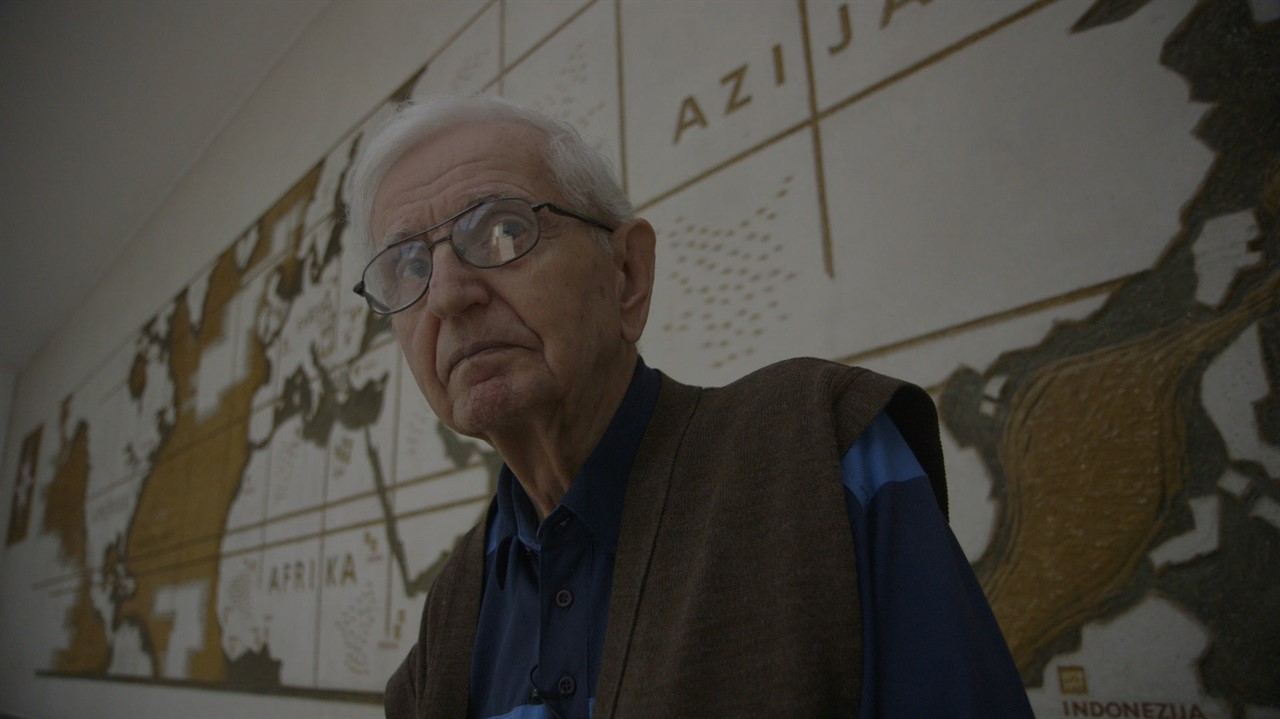 Elderly man in front of a long map of the word