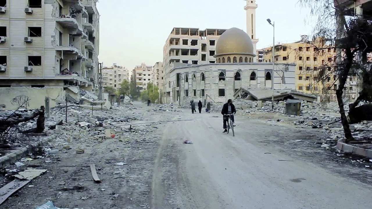 a person riding a bike by demolished buildings