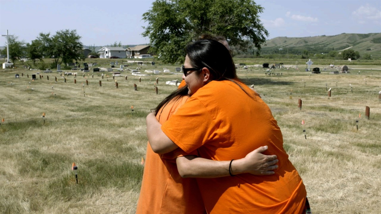 Woman in orange shirts hugging in graveyard