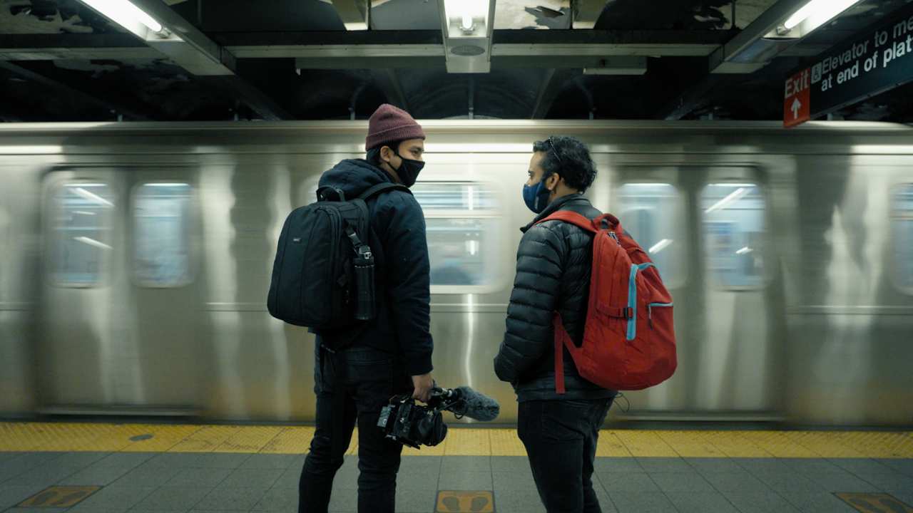 two men with a camera waiting for a subway