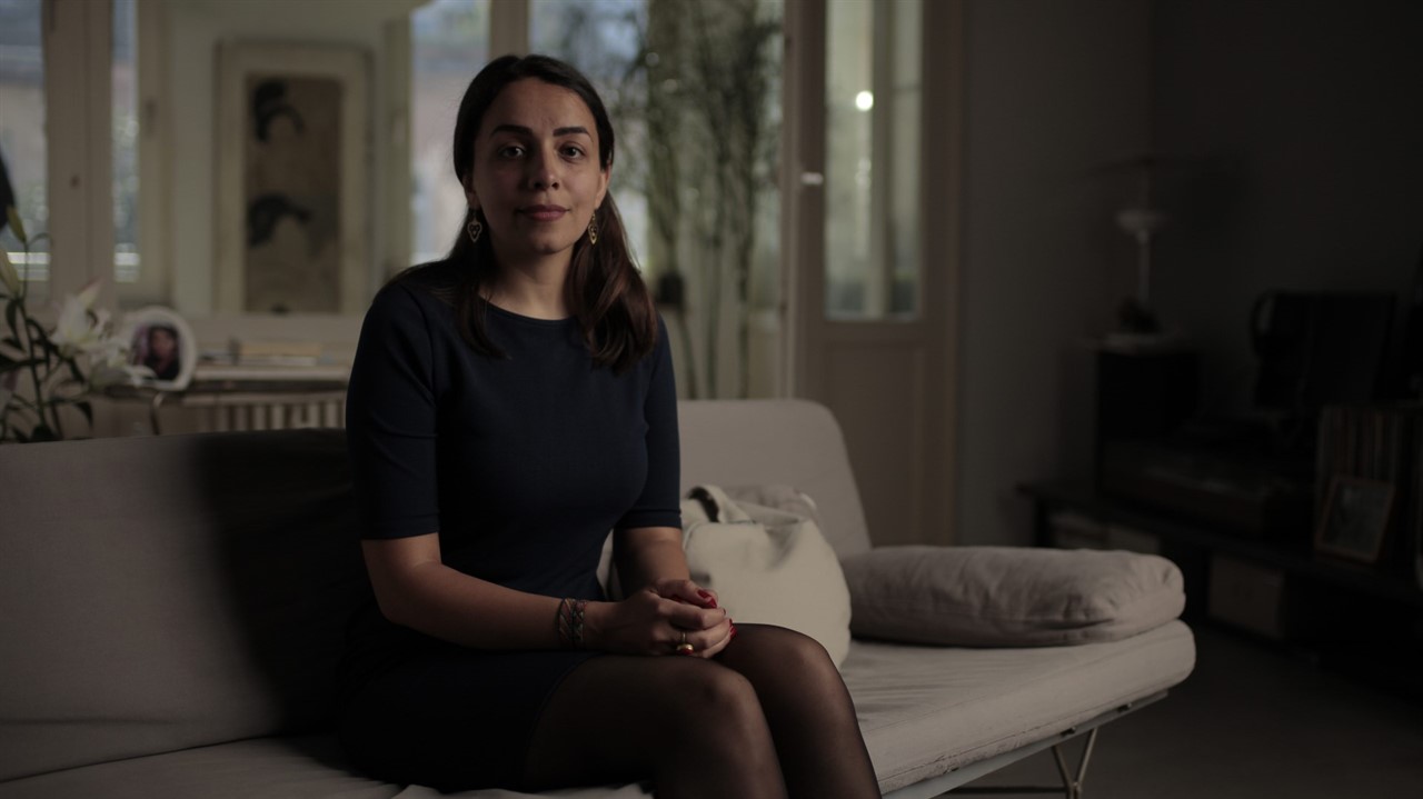 A woman sits with her hands in her lap on a couch