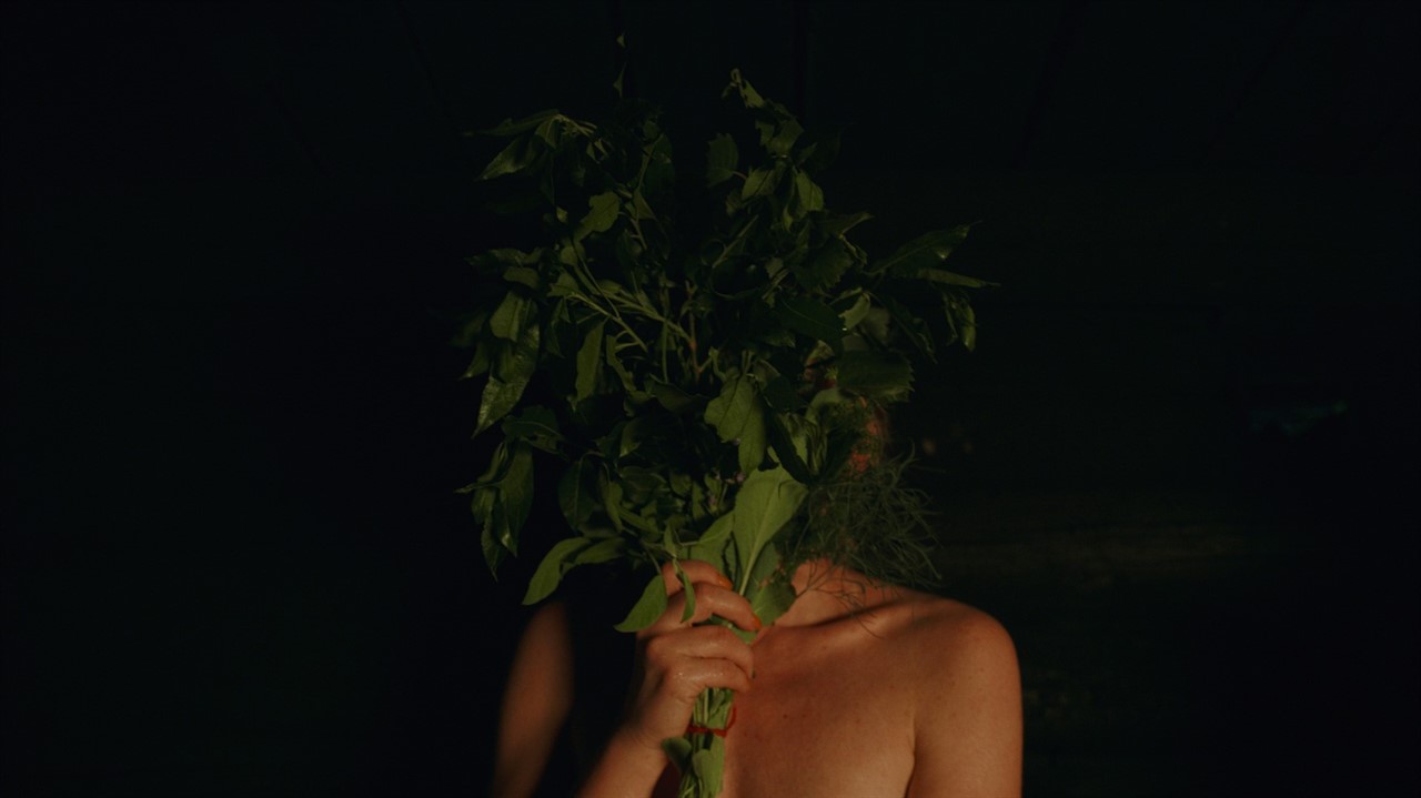 A topless person stands holding a bouquet of plant