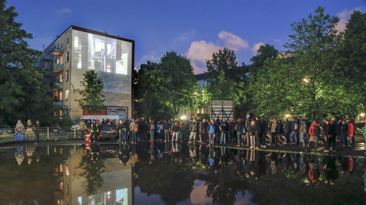 A large group of people watch an image projected o