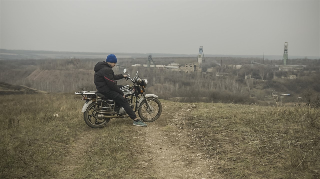 Man sitting on a motorbike overlooking industrial 