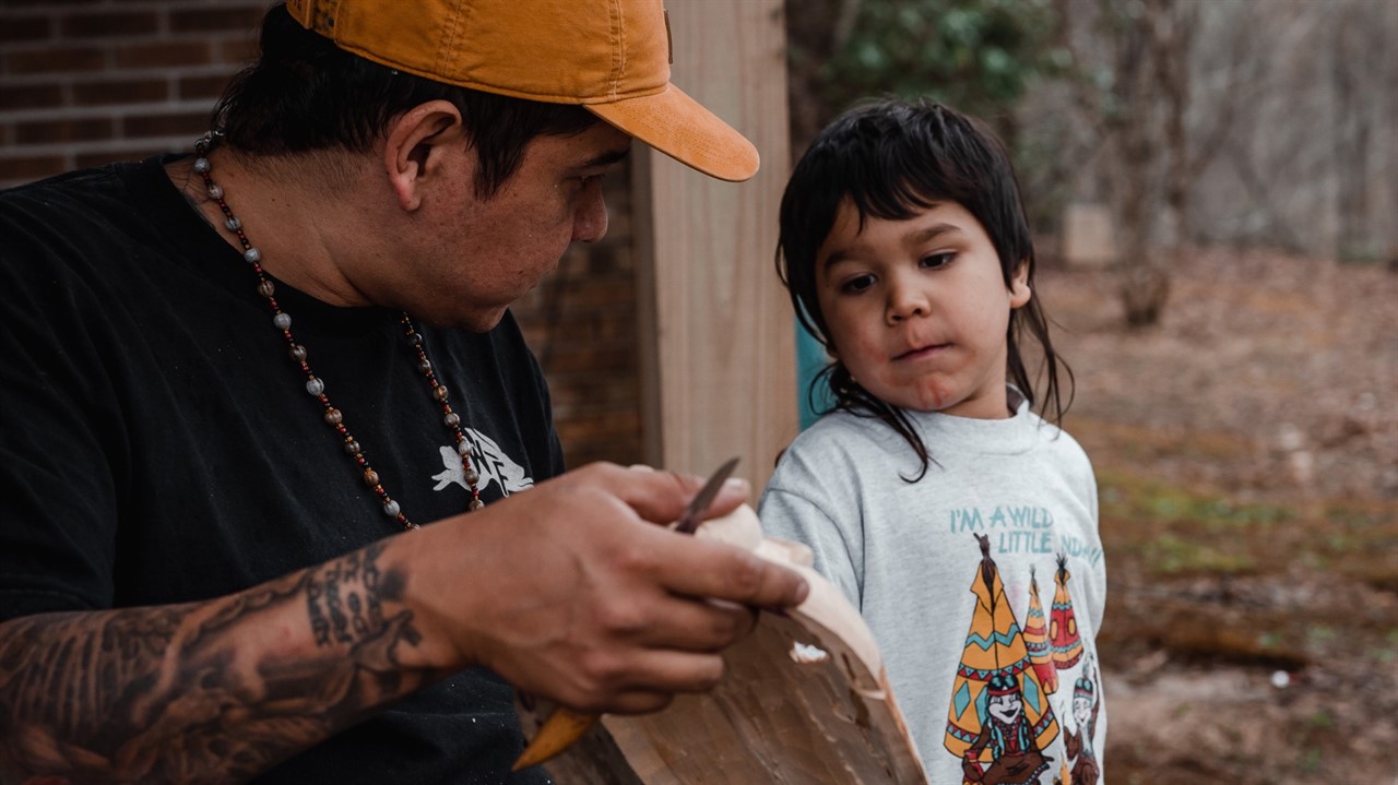 Indigenous man showing young chaild a carving