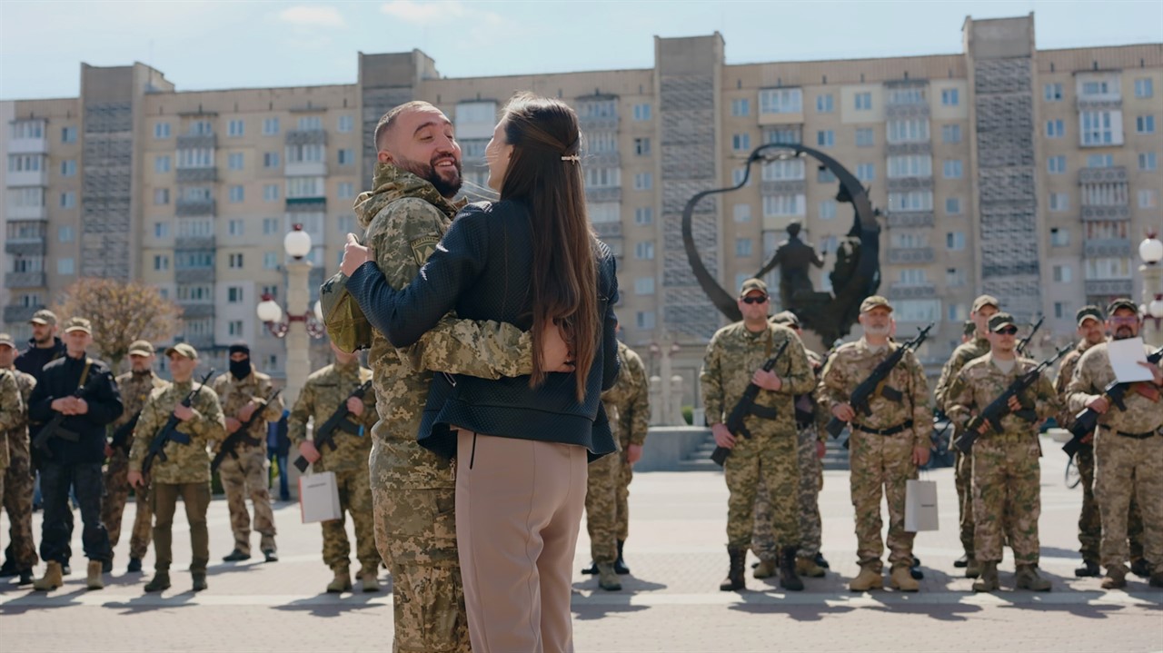 A couple, one in military fatigues, hug in front o
